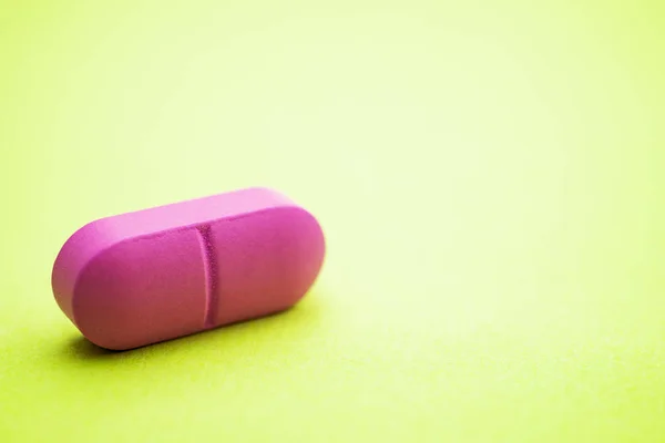 Pink pill on a green background — Stok fotoğraf