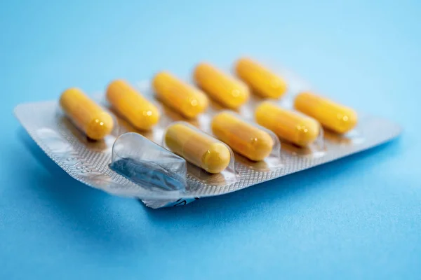 Žluté pilulky v blistrech balení na modrém pozadí — Stock fotografie