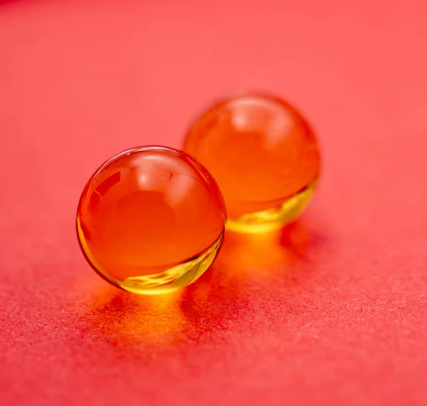 Two Transparent Capsules Fish Oil Red Background — Stock Photo, Image