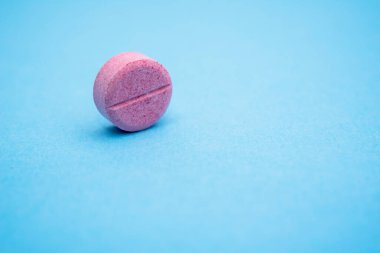 Kaburgaya bir tane yuvarlak pembe hap, mavi arkaplanı kapat.