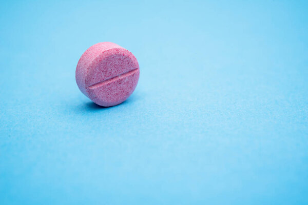 one round pink pill on the rib, close up blue background
