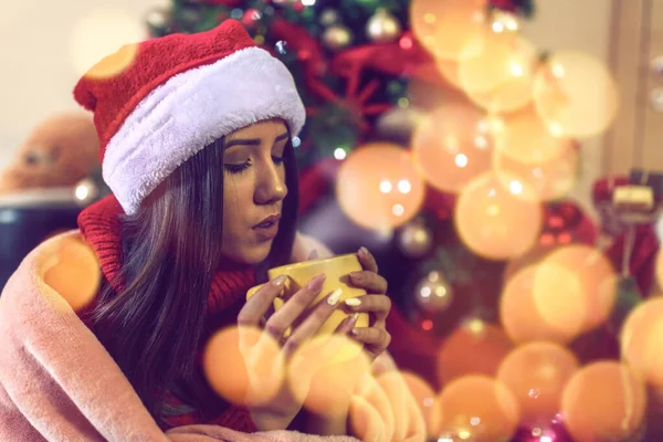 Noel Baba şapkalı genç kız evdeki Noel ağacında çay ya da kahve içiyor. — Stok fotoğraf