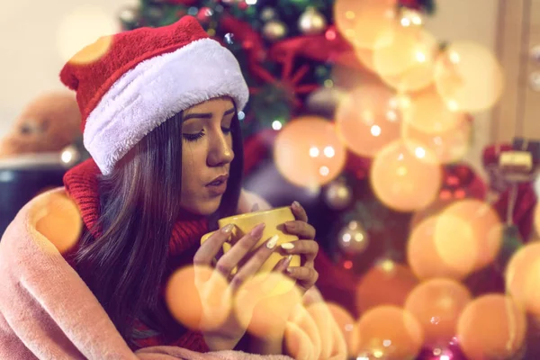 Young girl in Santa hat drinking tea or coffee over christmas tree at home — Stock Photo, Image