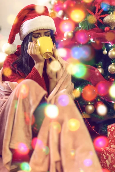 Mujer sentada junto al árbol de navidad y bebiendo té caliente —  Fotos de Stock