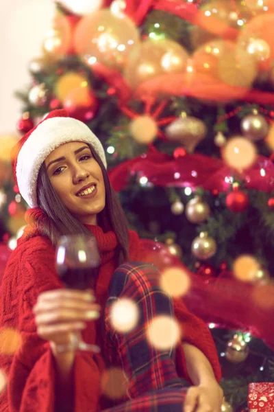 Frau stößt mit Rotwein an.Feiertage, Winter und Leute mit Weihnachtsmütze am Weihnachtsbaum zu Hause. — Stockfoto