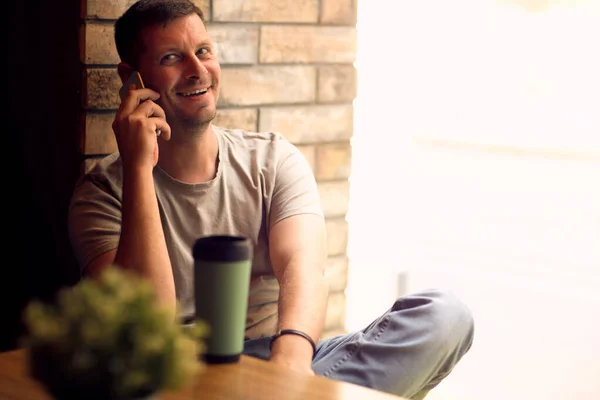 Hombre sonriente usando teléfono inteligente en cafe.Man relajarse en la cafetería. Freelancer . — Foto de Stock
