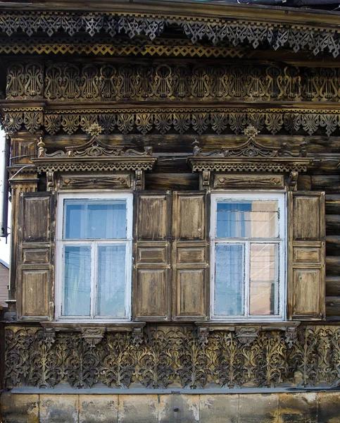 Dos ventanas con el arquitrabe tallado en madera en la antigua casa de madera en el casco antiguo ruso . — Foto de Stock