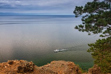 Bulutlu bir günde küçük gemi ile Deniz Baykal yukarıda çam ağacı