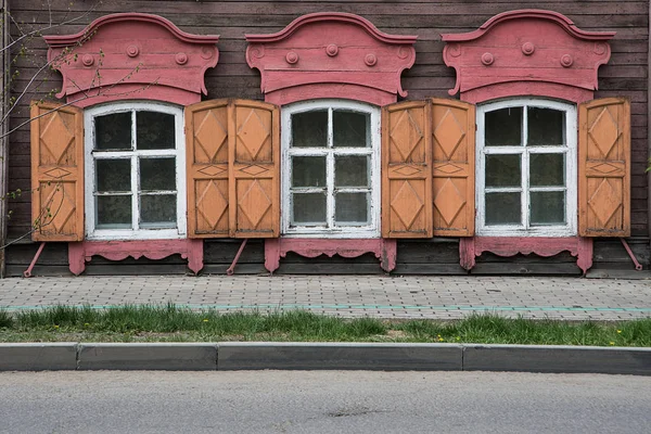 Tres ventanas con el arquitrabe tallado en madera en la antigua casa de madera en el casco antiguo ruso . — Foto de Stock