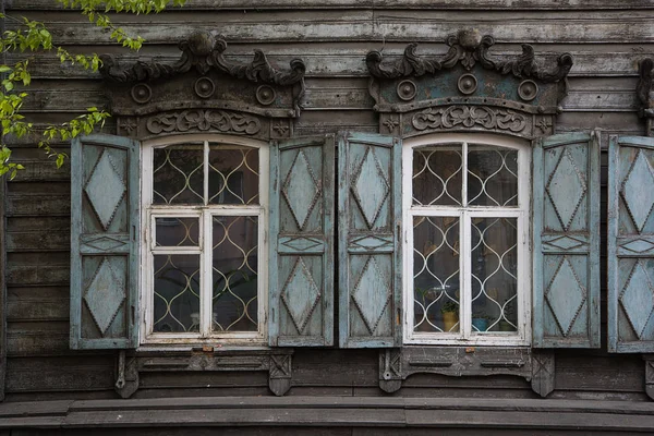 Two windows with the wooden carved architrave in the old wooden house in the old Russian town. — Stock Photo, Image