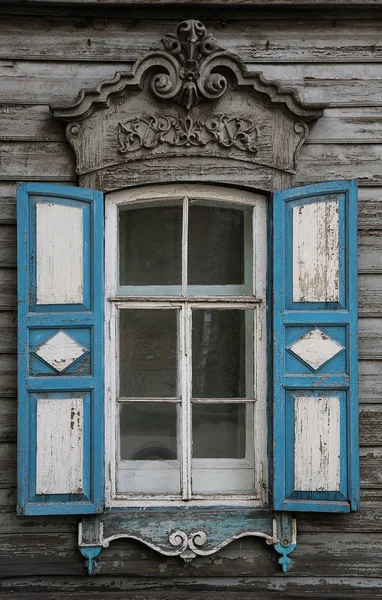 The window with the wooden carved architrave in the old wooden house in the old Russian town. — Stock Photo, Image