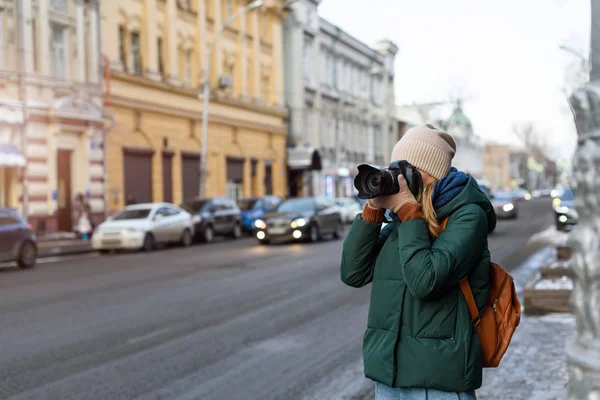 Fille en vêtements d'hiver avec appareil photo dans le centre historique de la ville prend des photos tout en visitant la ville . — Photo