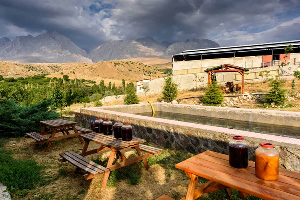 Village close the Turkish national Park aladag with mountain background behind with clouds on the sky and jar with cherry wine on the table, Turkey — 스톡 사진