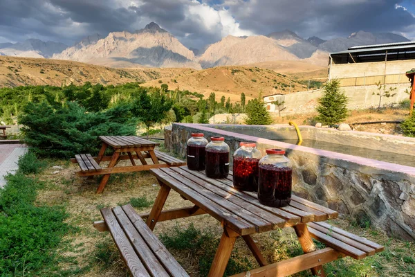 Village close the Turkish national Park aladag with mountain background behind with clouds on the sky and jar with cherry wine on the table, Turkey — 스톡 사진