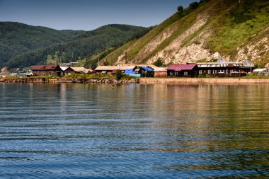 Baykal Gölü, Port Baykal yakınlarındaki köy, Rusya. Yüksek sahil manzarası, yeşil orman, evler, temiz göl suyu.