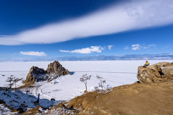 러시아 바이칼호: 2020 년 3 월 11 일: 소녀는 화창 한 행진 날 올 혼 섬 샤만 카 록에서 버 한 곶을 바라본다. 아름다운 구름이 덮인 바이칼호 — 스톡 사진