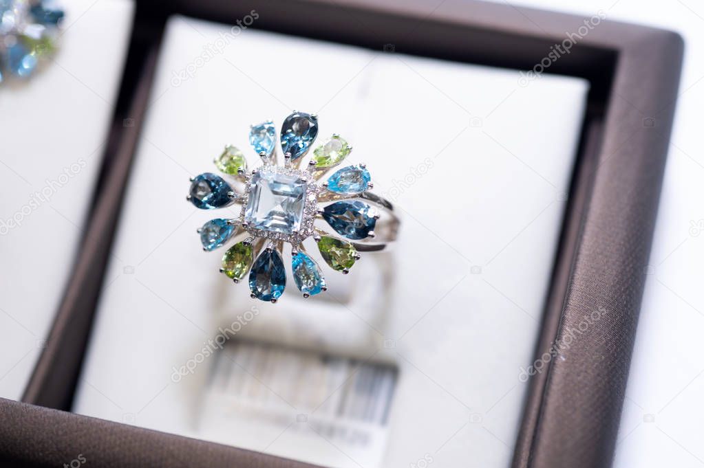 jewelry retail store showcase displaying white gold ring  with precious  gemstones. ring with huge sapphires, topazes diamonds, emeralds. close up