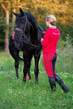 Biniciler gibi giyinmiş, siyah atlı kadınlar yeşil çayırda poz veriyor..