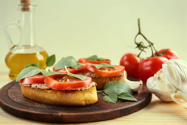 Bruschetta com patê de fígado, tomates e manjericão em uma tábua de madeira . — Fotografia de Stock