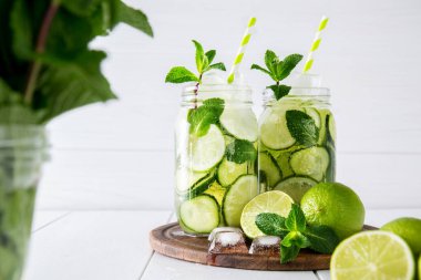 Meyve ve bitki su salatalık, kireç ve beyaz zemin üzerine nane ile aşılanmış. Detoks ve kilo kaybı kavramı.