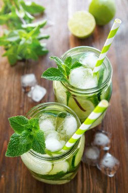Su iki kavanoz meyve ve bitki infüzyon ile salatalık, kireç, ahşap bir masa üzerine nane ve buz parçaları. Detoks ve kilo kaybı kavramı.