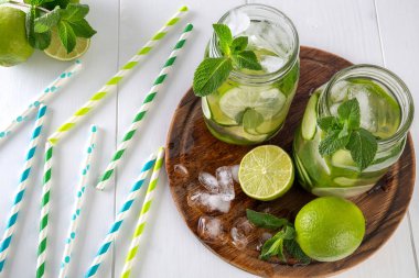 Su iki kavanoz meyve ve bitki infüzyon ile salatalık, limon, nane ve buz parçaları bir ahşap tahta üzerinde. Kokteyl kağıt rulo bir tablo üzerinde dağınık vardır. Detoks ve kilo kaybı kavramı.