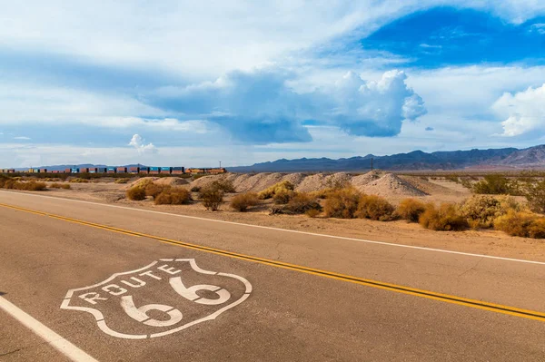 U.S. Rota 66 rodovia, com sinal no asfalto e um longo trem no fundo — Fotografia de Stock