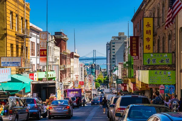San Francisco - September 20, 2015: Downtown city life in a busy street of Chinatown San Francisco. View with many people, shops and cars - lookout to the Oakland Bay Bridge. — Stock Photo, Image