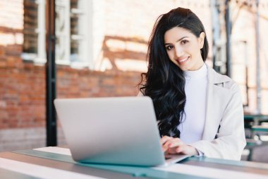 Çekici kadın blogger açık kafede otururken modern dizüstü bilgisayar kullanarak yeni zorlu yazı yazarak. Güzel esmer işkadını onun iş projesi yapmak laptop ile çalışma