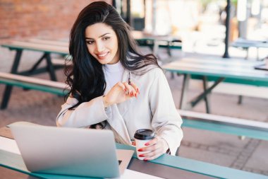 Açık kafe paket servisi olan restoran kahve holding genel dizüstü bilgisayar önünde oturan genç serbest meslek esmer kadın zevk ücretsiz kablosuz internet bağlantısı sevindim. Gevşeme, güzellik ve gençlik kavramı