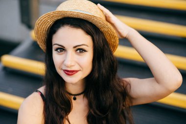 Koyu renk gözleri ve güzel makyaj emin göz olan merdiven oturan Hasır Şapkalı olan saç ile güzel bir kadın. Kameraya poz görünüm çekici ile çekici esmer Bayan