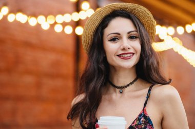 Siyah uzun saçlı, ela gözlü ve kırmızı dudaklar, kolye, yaz şapka ve açık café'de poz süre hoş ifade sahip elbise giyen genç kadın modeli. İnsanlar, dinlenme, duygular kavramı