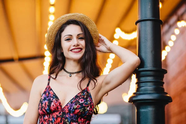 Fashionable elegant woman wearing dress with flower print and straw hat, posing at camera with smile, feeling relaxation, having good mood. People, beauty, lifestyle, facial expression, youth concept