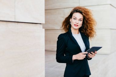 Onun iş ortağı yakın kafe, bekleyen elinde, tablet tutan zarif elbiseler giymiş güzel işkadını kıvırcık kabarık saçlı ücretsiz internet conncection kullanarak. İnsanlar, kariyer, iş