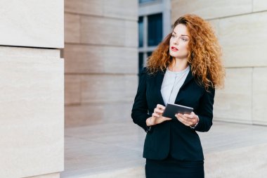 Onun çalışma günü planlama kadın girişimci kıvırcık gür saçlı resmi elbise giyiyor, modern tablet holding, dalgın bir ifadeyle bir yana, arıyorum. Dokunmatik yüzey kullanarak proje geliştirme kadın