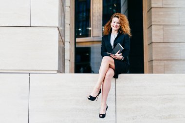 İyi bir ruh hali onu dizüstü ve tablet, onun iş ortakları ile biranlaşma tutarak siyah resmi kostüm ve yüksek topuklu ayakkabılar giyen genç çekici Bayan kıvırcık saçlı olan