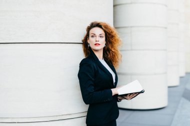 Çok şık kadın kıvırcık dalgalı saçlı siyah takım elbiseli, onun gelecek planları üzerinde düşünme cep kitabı bir kenara mesafe içine arıyorum elinde tutan giyinmiş. Moda Bayan yazma gerekli notlar