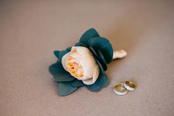 Rosa beige artificial y anillos de boda tumbados sobre fondo blanco y suave. Detalles de la novia. Composición de los accesorios de la novia. Anillos de oro de pareja feliz va a casarse — Foto de Stock