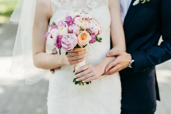 Schnappschuss der schönen Braut im weißen Brautkleid, die einen Strauß in der Nähe des Bräutigams hält, der sie von hinten umarmt. glückliches Brautpaar. Hochzeitspaar. schöne Blumen in den Händen der Braut — Stockfoto