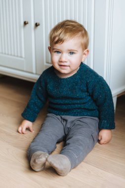 Dikey bebek portresi dolap yakın katta oturur, sıcak mavi gözleri ile görünüyor. Çocuklarla oynamak için güzel sarışın bebek erkek olacak kapalı atış. Merakla içine kamera küçük yürümeye başlayan çocuk bakmak