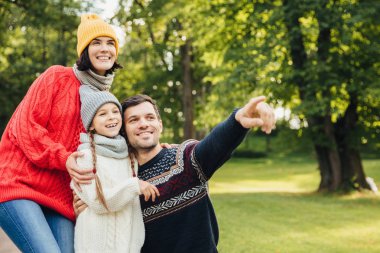 Aile, sezon, ilişki kavramı. Dost sevgi dolu aile sonbahar parkında yürüyüşler, güzel doğaya hayran, sıcak örme giysiler giymek, mesafe gösterisi olarak içine ilginç bir şey işaret