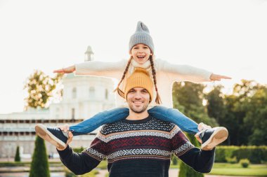 Genç yakışıklı baba sırtıma küçük gülümseyen kızı verir, birlikte gezi varken eğlen. Küçük çocuk, babasının arkada olurken horizont görünüyor. Adam kız yolculuk geri verir