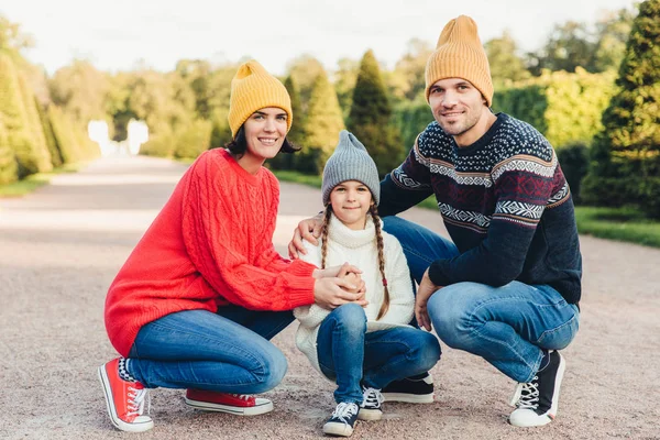 Friendly family wear knitted clothes, have walk together, admire splendid autumn weather. Affectionate young parents and their little cute daughter play together outdoor. Relationship concept