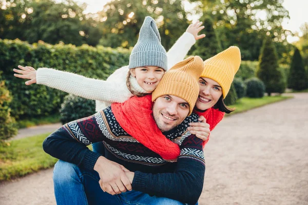 Divertirmo-nos juntos! Sorrindo excitado mulher, homem e sua criança pequena fêmea, use roupas de malha quente, abraçar uns aos outros, andar no parque, estar de bom humor. A família dá apoio, encorajamento — Fotografia de Stock