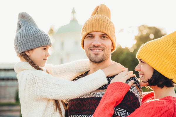 Piękne małe dziewczyny cieszyć się razem z rodzicami, objąć jej ojca z wielką miłością, razem spędzają weekendy jesień. Zrelaksowany młodych ludzi w kapelusze mają happy wyrażeń. Pojęcie Wspólnoty — Zdjęcie stockowe
