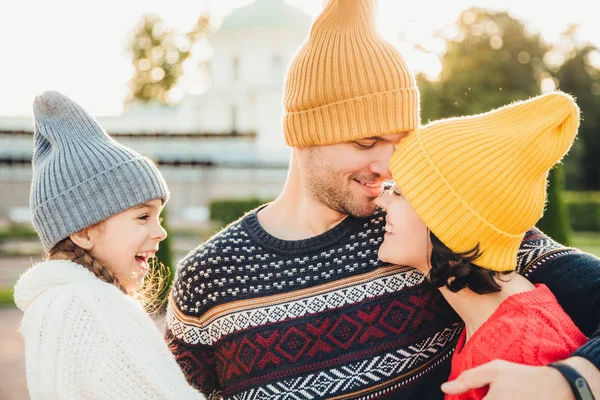 Criança pequena excitada olha para seus pais que estão apaixonados, indo beijar um ao outro, ter relacionamentos goos, abraçar. Mulher afetuosa e apoio do homem. Sorrindo menina olha para o pai ea mãe — Fotografia de Stock