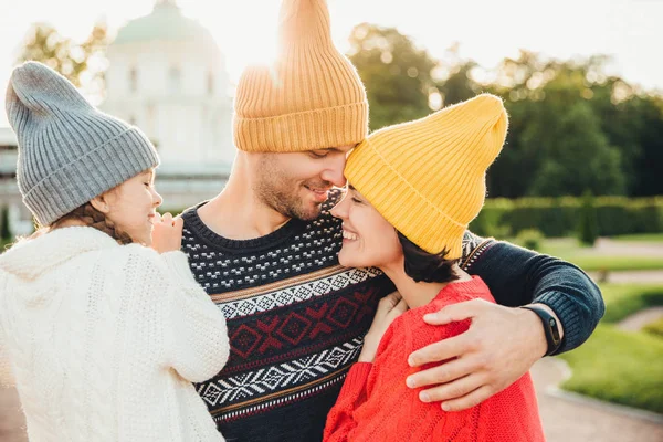 매력적인 남자 노란색 따뜻한 모자를 착용, 그의 아내와 딸을 포용, 위대한 사랑으로 그들에 보인다. 사랑 스러운 소녀 느낌 부모, 아버지의 손에 있는 동안 행복 하 게 미소에서에서 지원 — 스톡 사진