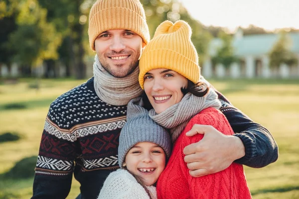 Criança adorável ficar perto de seus pais afetuosos, desfrutar de passar o tempo juntos, abraçar uns aos outros, sorrir feliz, olhar diretamente para a câmera. Momentos inesquecíveis agradáveis com a família — Fotografia de Stock