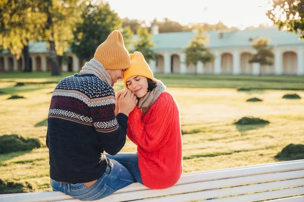 진정한 감정을 고 romantisism 개념. 노란색 니트 모자와 빨간색 따뜻한 스웨터에 사랑 스러운 젊은 여자 남자 친구의 손에서 그녀의 손을 따뜻하게, 함께 벤치에 앉아, 눈 큰 즐거움을 — 스톡 사진