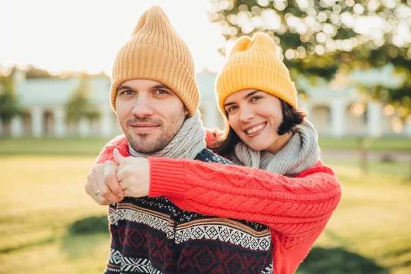 Uśmiechający się zadowolony, że młoda kobieta w kapelusz i ciepły sweter z bawełny obejmuje jej męża, który w pewnym oddaleniu, razem spędzać weekendy, spacer w ogrodzie lub parku, podziwiać wspaniała słoneczna pogoda jesienią — Zdjęcie stockowe